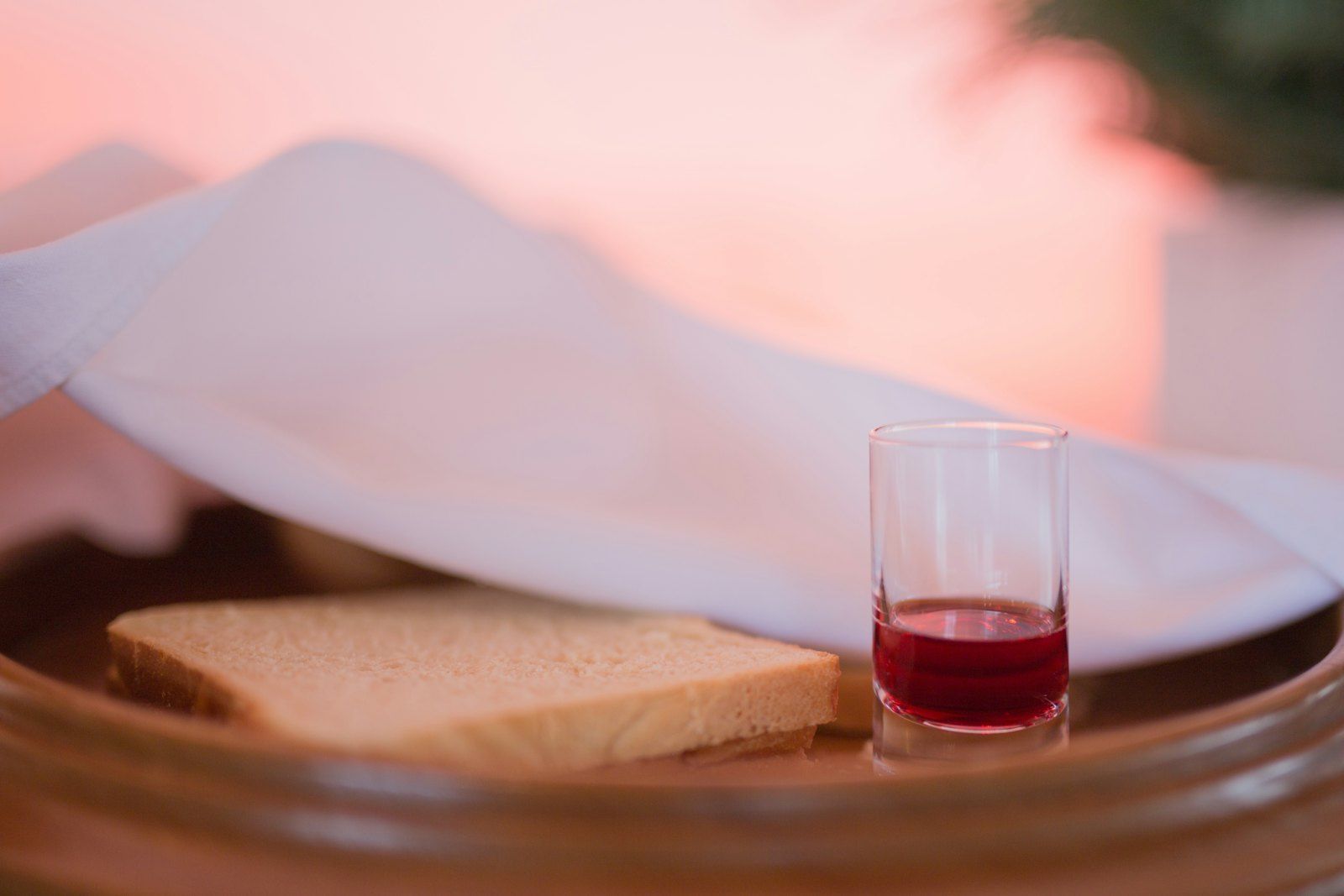 A small loaf of bread and a cup of fruit of the vine on a tray, prepared for the Lord's Supper